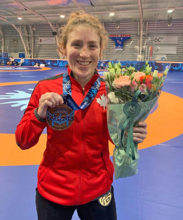 Samantha Stewart wears her bronze medal around her neck and holds it up with her right hand while holding flowers in her left hand.