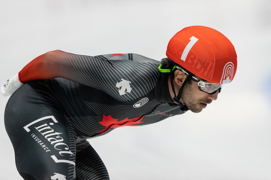 Close up image of speed skater on the ice. It is a side profile shot, the skater is hunched over looking forward with hands clasped behind their back.