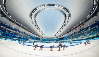 Wide shot of Canadian speed skaters rounding the ice