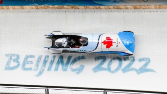 Two person bobsleigh goes past Beijing 2022 sign on ice track