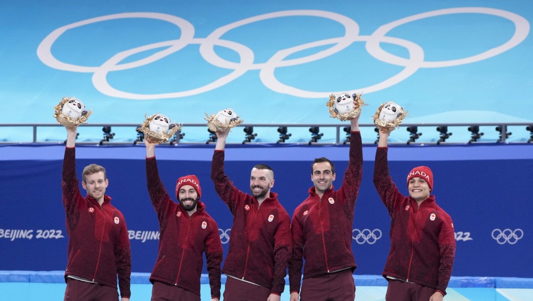 Five Canadian short track speed skaters hold mascots above their heads on the podium