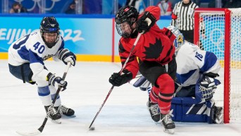 Sarah Fillier #10 of Team Canada tips the puck while avoiding a check by Noora Tulus #40 of Team Finland during the Beijing 2022 Olympic Winter Games