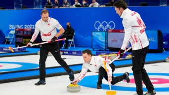 Brad Gushue throws a stone with Geoff Walker and Brett Gallant ready to sweep