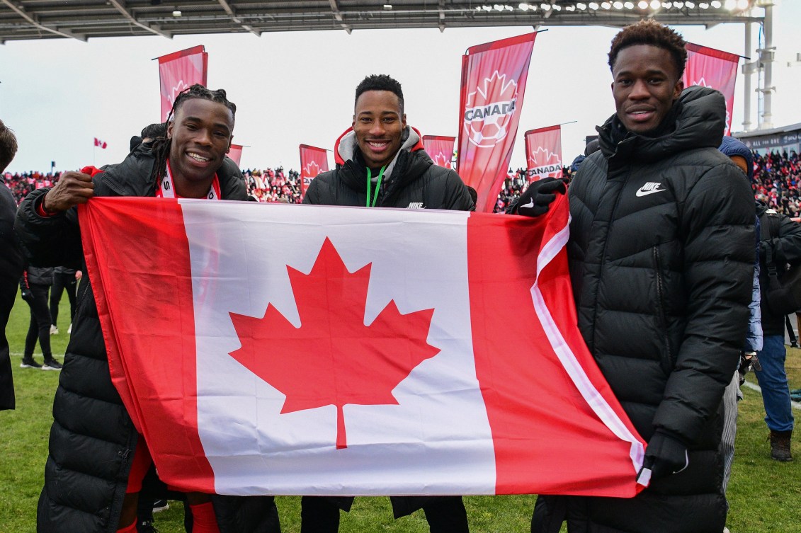 Samuel Adekugbe, Mark-Anthony Kaye, Iké Ugbo hold a Canadian flag 