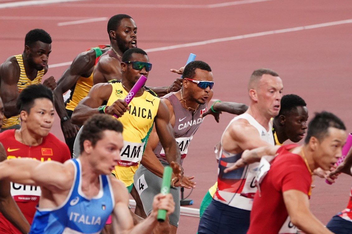 A lot of male sprinters make baton exchanges in a relay race