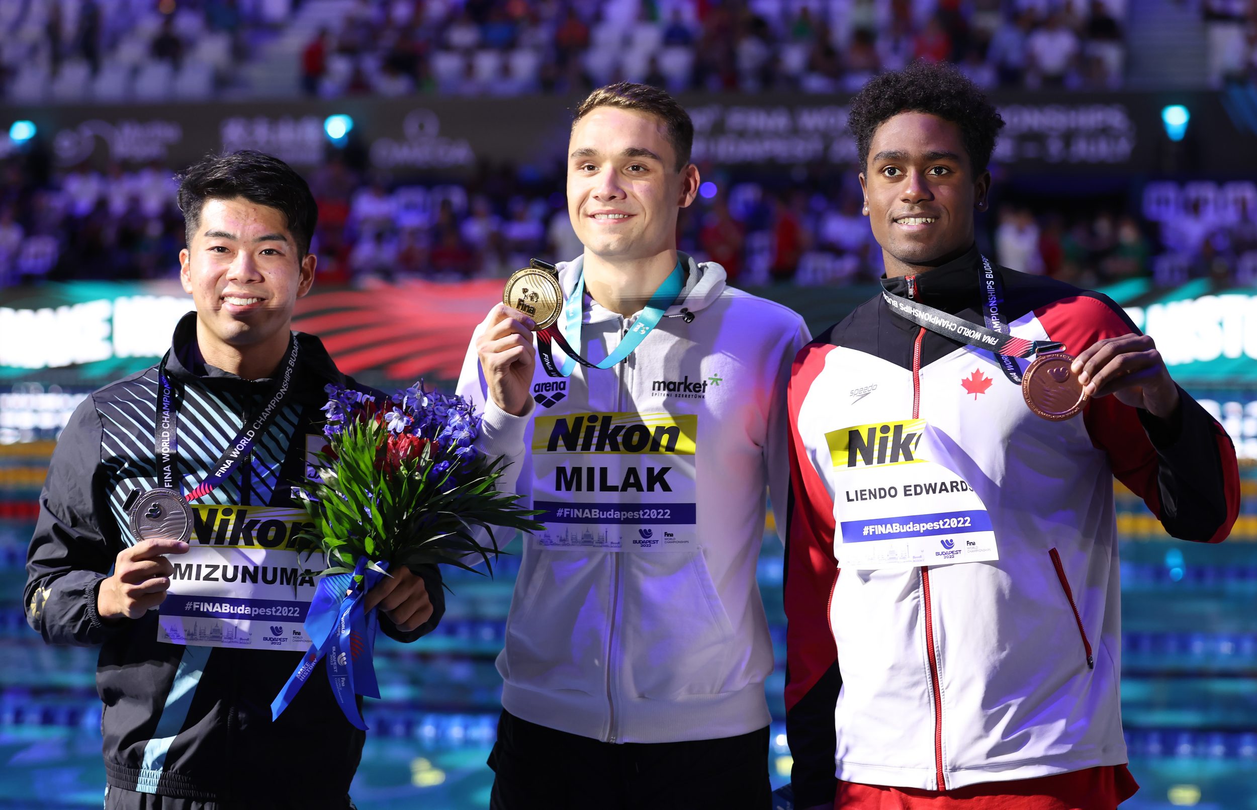 Joshua Liendo holds up his bronze medal while standing alongside his fellow medallists