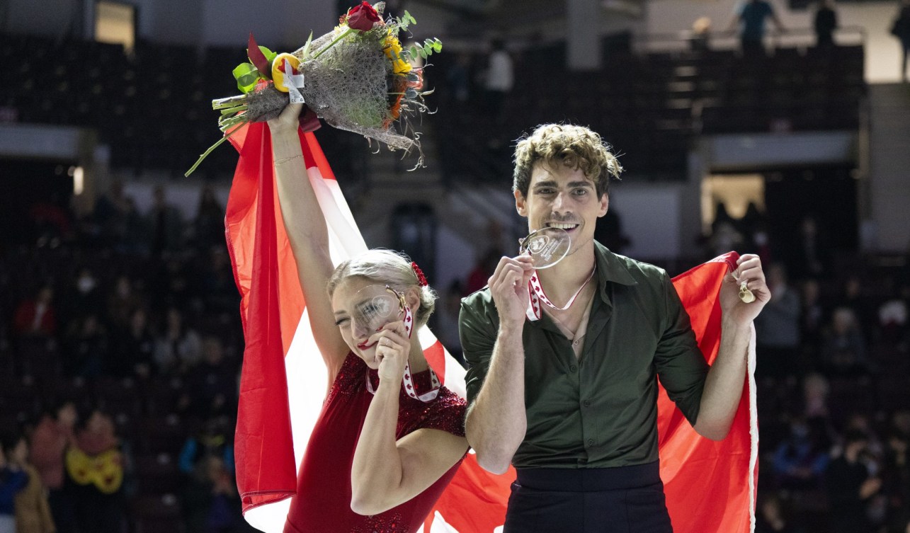 Piper Gilles holds her medal to her eye like a magnifying glass while Paul Poirier bites his medal