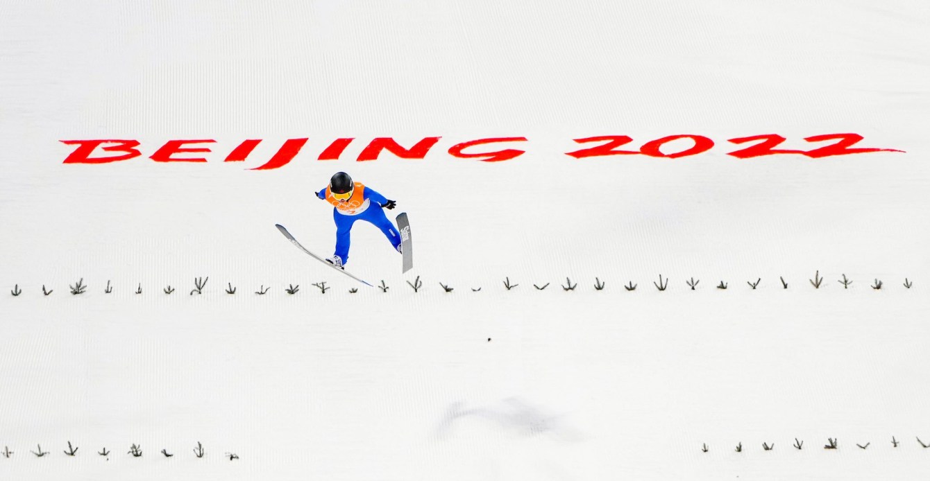 Abigail Strate performs a ski jump with her skis in V shape with white snow as backdrop