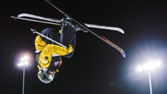Brendan Mackay upside down in the air with a black sky behind him performing a ski trick