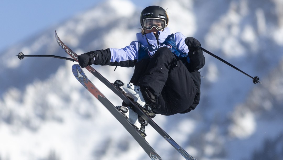 Megan Oldham grabs her ski while doing a trick with a mountain in the background