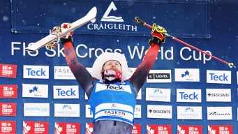 Brady Leman raises his skis and poles above his head in celebration on the podium