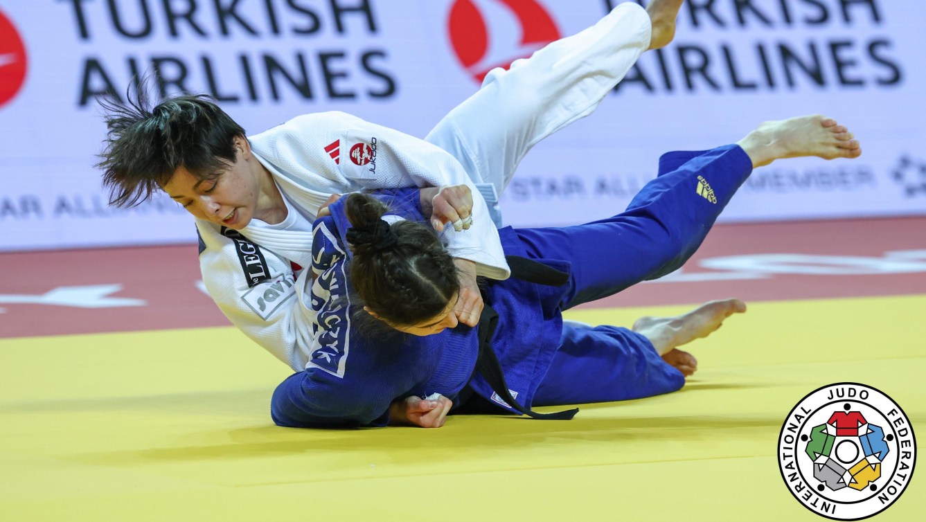 Christa Deguchi in a white outfit takes her opponent in blue to the judo mat