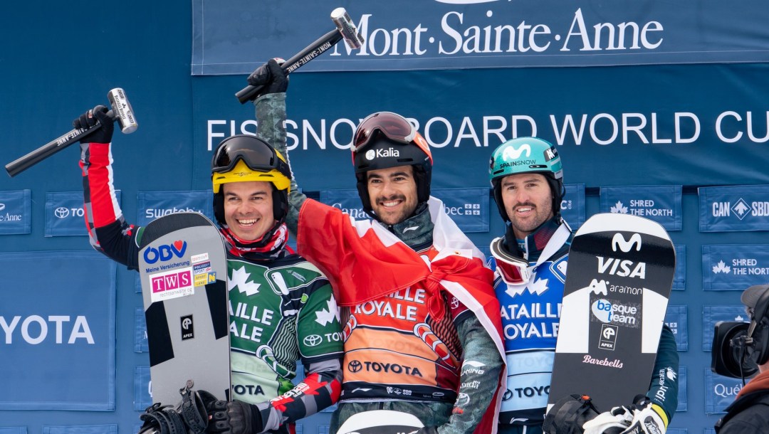 Three snowboarders stand on the podium holding hammers above their heads