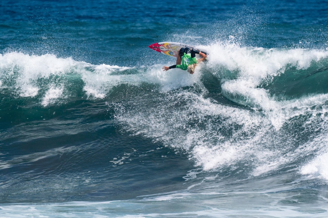 Erin Brooks is almost upside down while riding a wave on her surfboard 