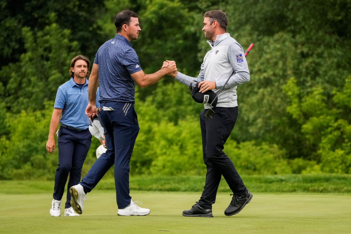 Corey Conners and Nick Taylor shake hands on a golf course