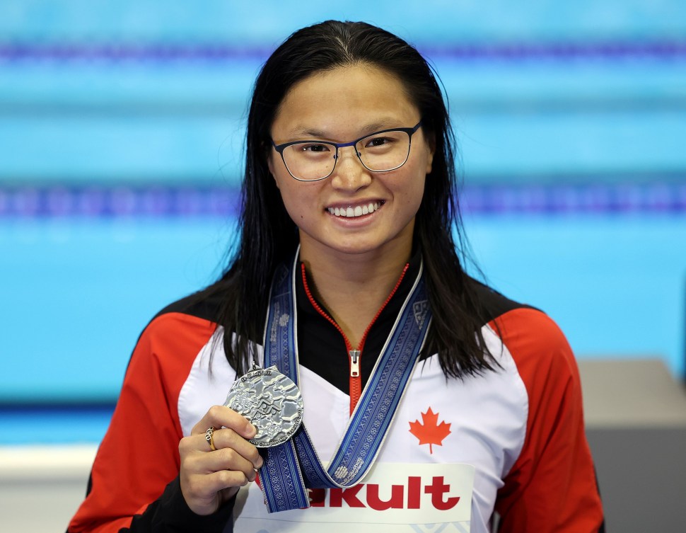 Maggie Mac Neil holds up her silver medal hung around her neck