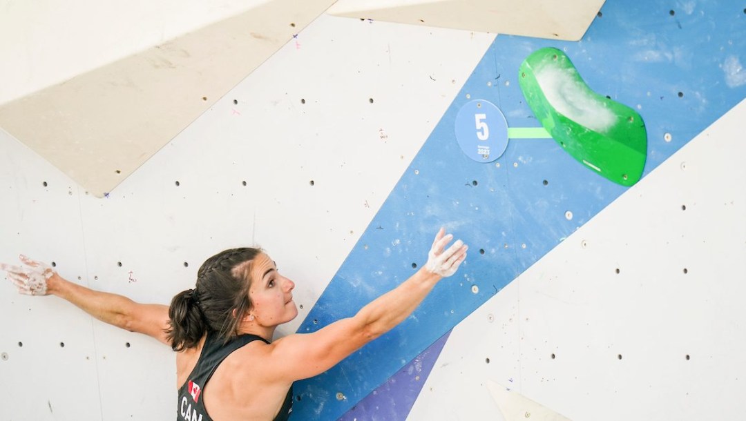 A sport climber reaches for a green hold on a wall
