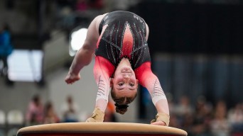 A gymnast in a black and red leotard backflips over a vault