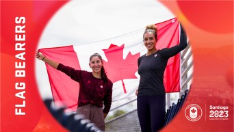 Melissa Humana-Paredes and Brandie Wilkerson smile and hold a Canadian flag between them.