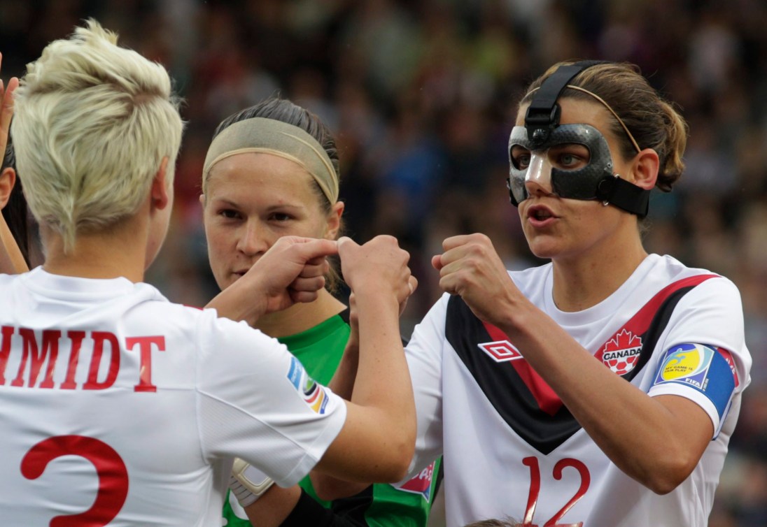 Christine Sinclair, wearing a protective mask, talks to teammates
