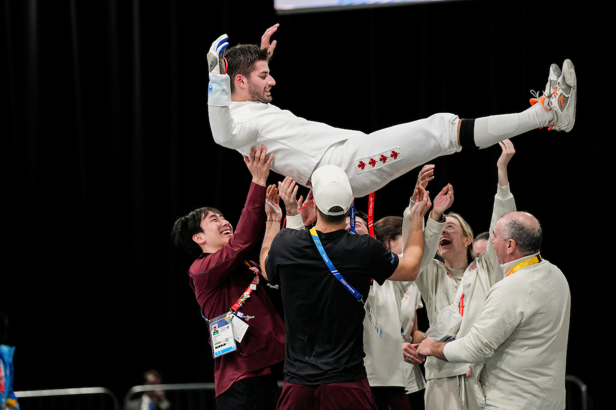 Dylan French in his fencing uniform is tossed in the air by his teammates and coaches
