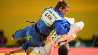 A judoka in blue takes a judoka in white down to the mat