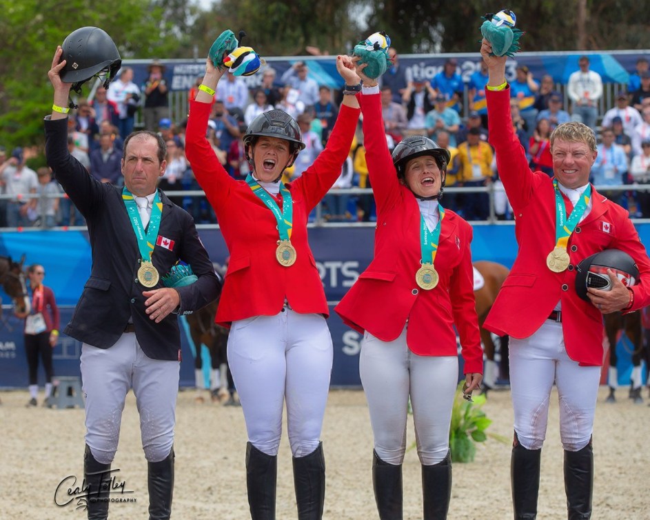 Four Canadian equestrians stand on the podium with gold medals and their arms in the air 