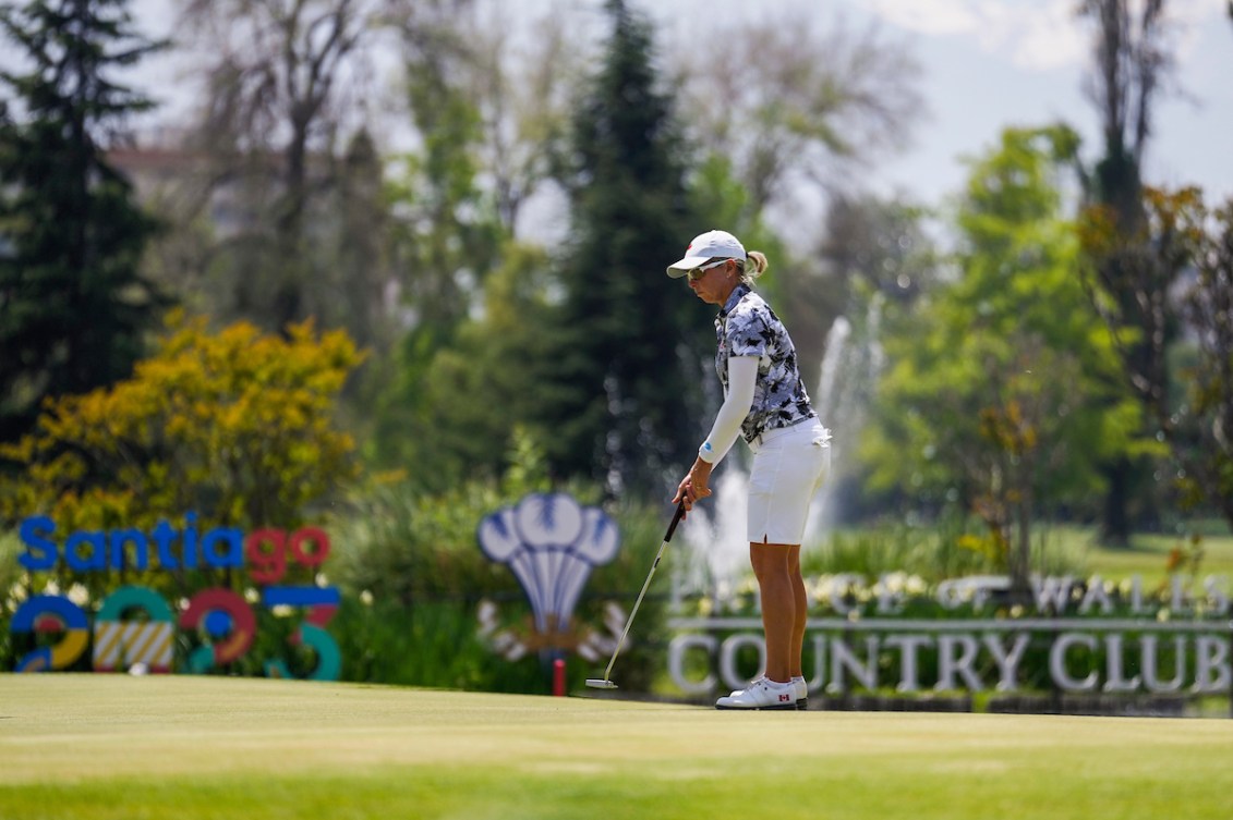 A female golfer for Team Canada wears all white and attempts to hit a ball.