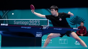 Edward Ly dressed in black hits a return shot in a table tennis match