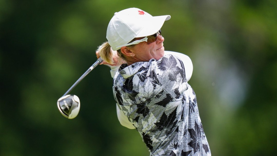 A female golfer for Team Canada wears all white and is in a backswing after making a golf shot