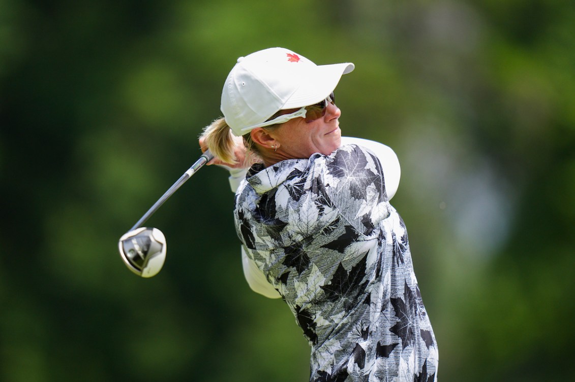 A female golfer for Team Canada wears all white and is in a backswing after making a golf shot