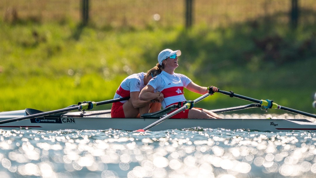 One rower leans forward to hug her teammate in front of her in the boat