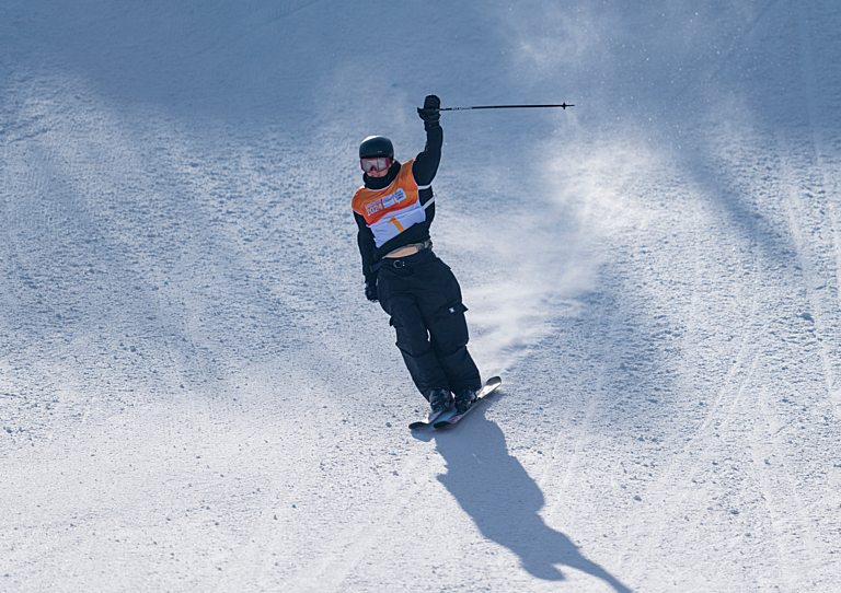 Skier raises one arm as he skis into the finish area