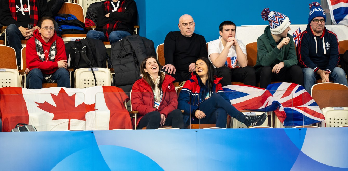 Lisa Weagle and Eve Muirhead laugh while sitting next to each other watching a curling match