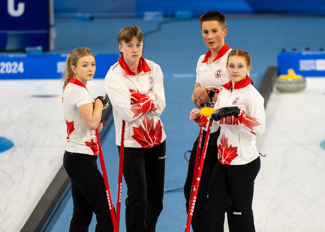 Four Canadian curlers chat on the side of the ice sheet 