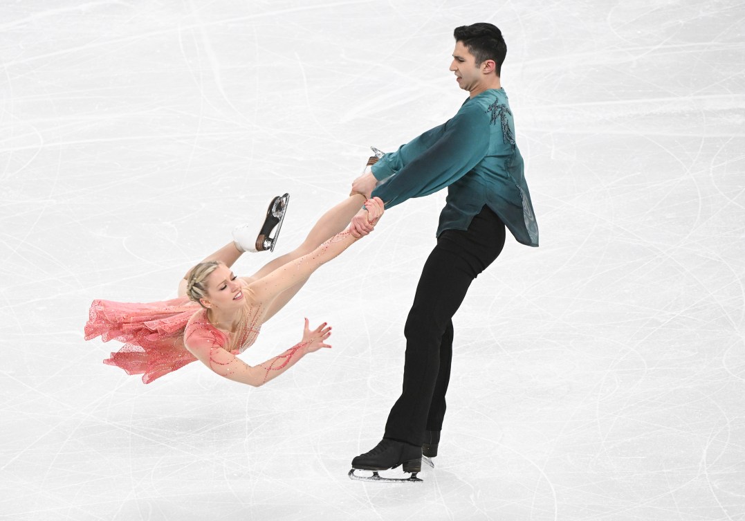 Zachary Lagha in a green shirt and black pants swings Marjorie Lajoie in a pink dress by her feet in a lift