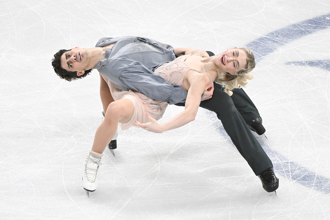 Piper Gilles and Paul Poirier glide on the ice leaned over each other's legs 