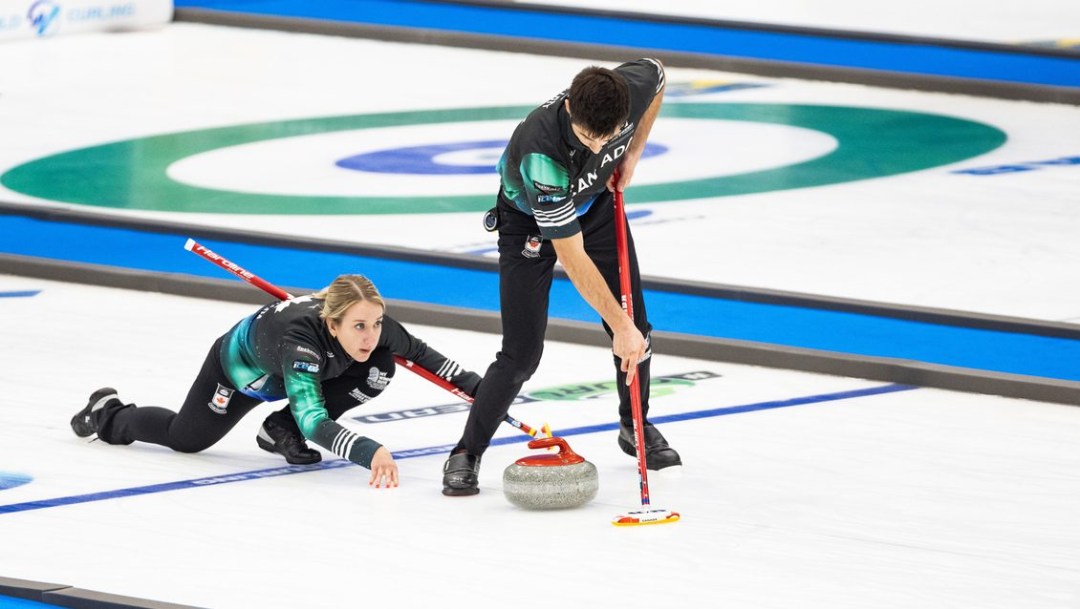 Kadriana Lott dressed in all black throws a red stone as Colton Lott sweeps in front of it