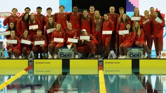 29 swimmers in their Team Canada lululemon track suits pose on the pool deck with Air Canada boarding passes