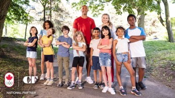 Athletes Damian Warner and Ellie Black stand with a group of children on an outdoor path