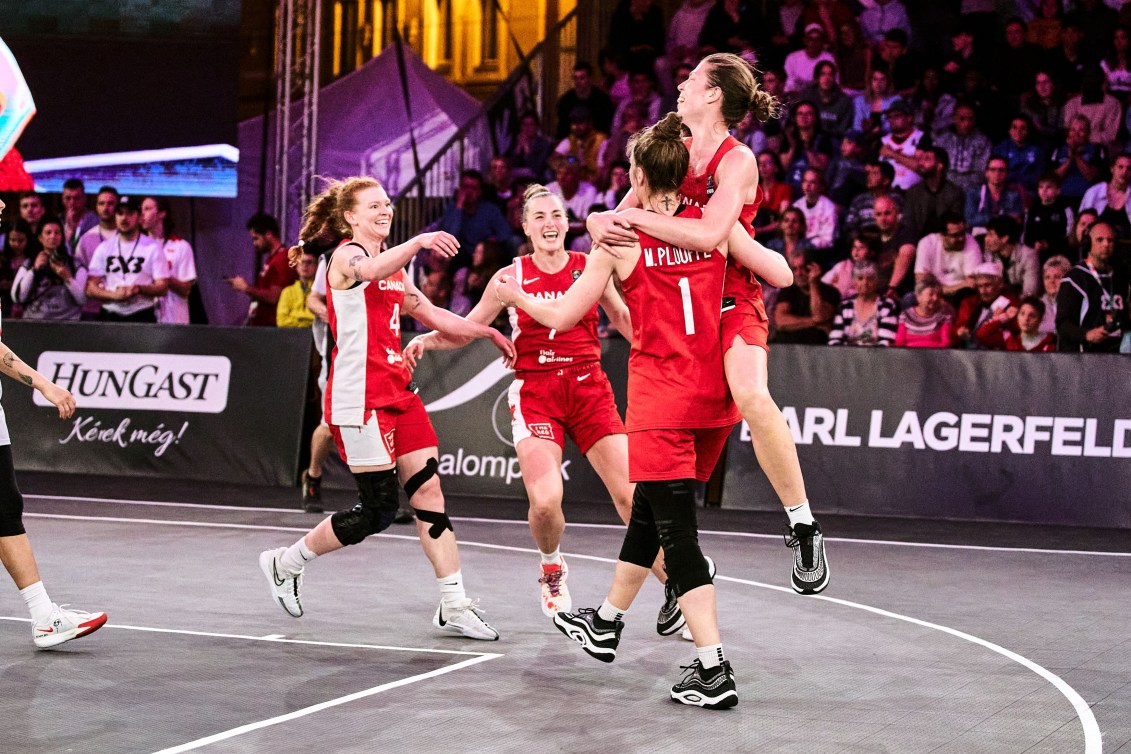 Four women basketball players in red uniforms run and jump at each other to hug 