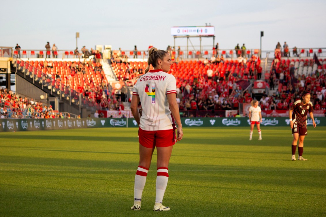 Shelina Zadorsky stands on the soccer pitch while wearing a pride jersey