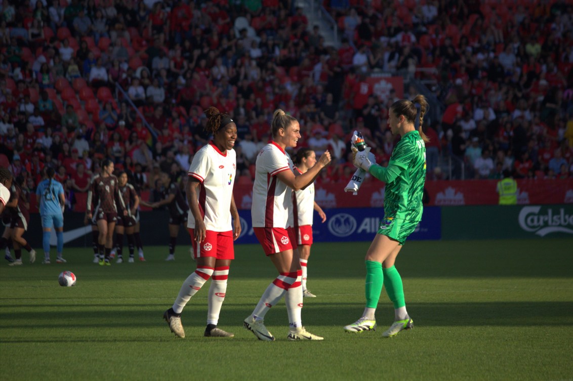 Team Canada soccer players celebrate together on the field.