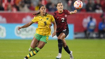 Sydney Collins in red chases after a Jamaican soccer player in yellow jersey