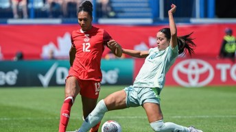 Jade Rose in a red soccer uniform fights for the ball against a player dressed in light green