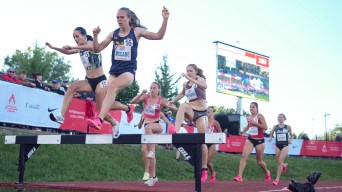 Women in a steeplechase race jump over the big hurdle