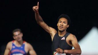 Christopher Morales Williams dressed in black holds his finger in the air for number one as he runs across a finish line