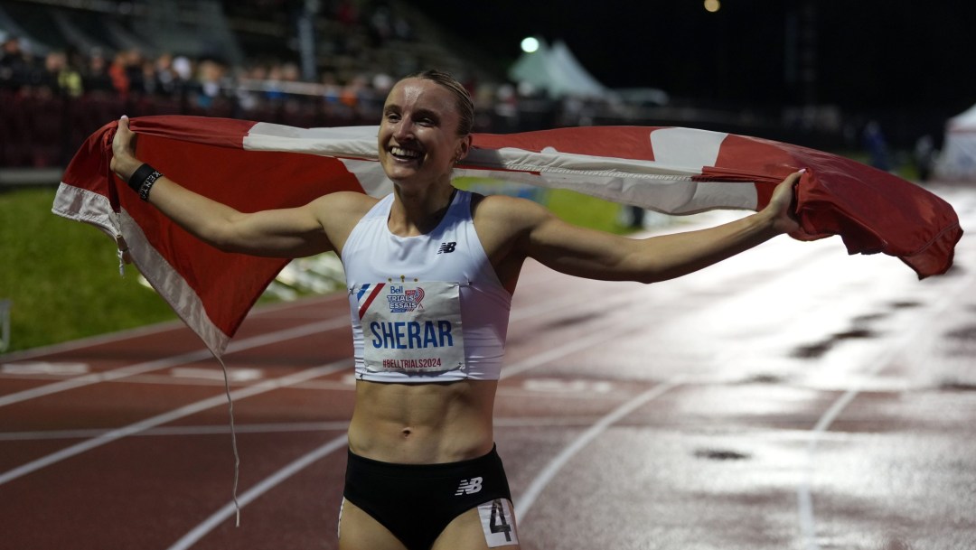 Zoe Sherar in white top and black shorts holds the Canadian flag out behind her on a dark wet night