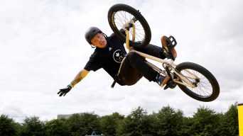 A BMX freestyle rider in black performs a trick with his hands off the handlebars