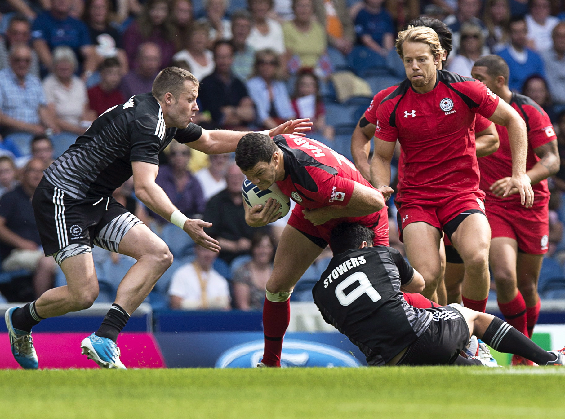 Canada's Ciaran Hearn is tackled by New Zealand's Tim Mikkelson, left, and Sherwin Stowers in Commonwealth Games rugby sevens action at Ibrox Stadium in Glasgow, Scotland on Saturday, July 26, 2014. New Zealand won 39-0. THE CANADIAN PRESS/Andrew Vaughan